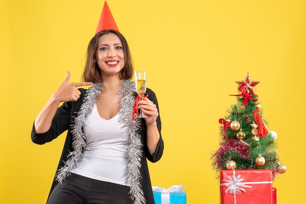 Kerstsfeer met verwarde mooie dame die wijn in het kantoor op geel houdt