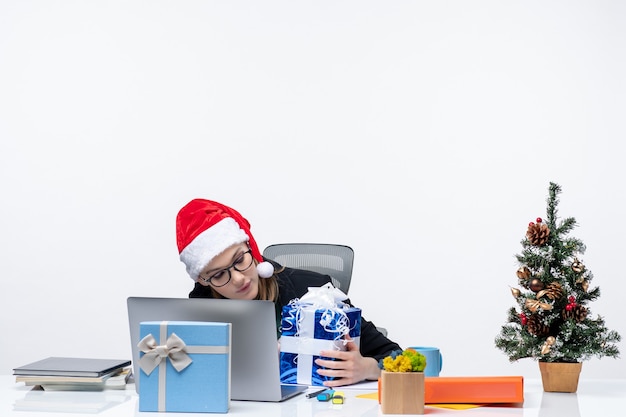 Kerstsfeer met zakenvrouw met kerstman hoed en bril zittend aan een tafel waar geschenken en versierde nieuwe jaarboom daarop op witte achtergrond