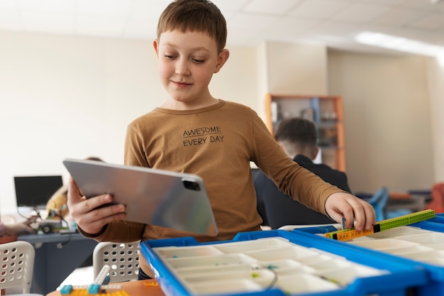 Kid controleert een elektronisch onderdeel en zijn tablet om een robot te bouwen