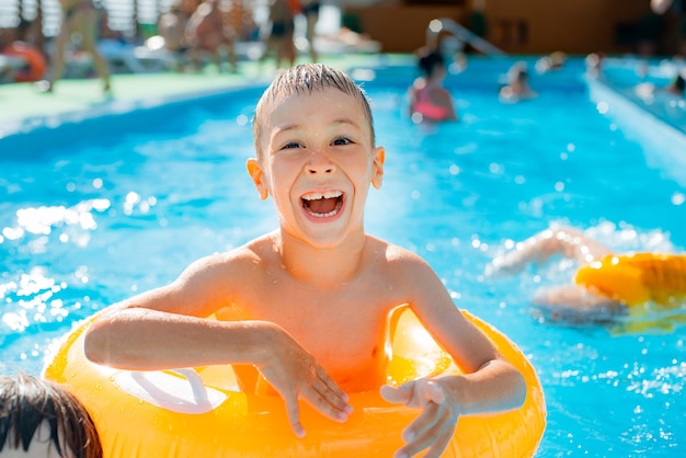 Kid jongen spelen buitenzwembad van resort. in een opblaasbare gele cirkel met een bal. kinderen ravotten met waterspeelgoed. rond spetterend. ontspan warmte.