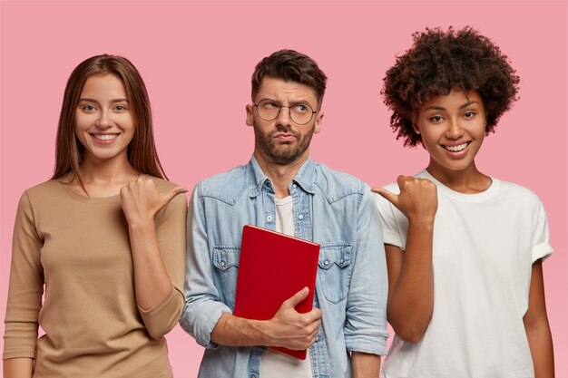 Kijk naar deze wonk! Vrolijke vrouwen wijzen met hun duim naar de man die tussen hen in staat