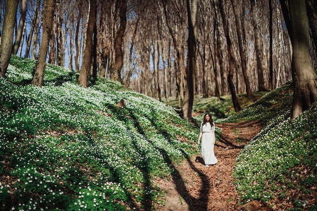 Gratis foto kijk van veraf naar de vrouw in het wit wandelen in het groene bos