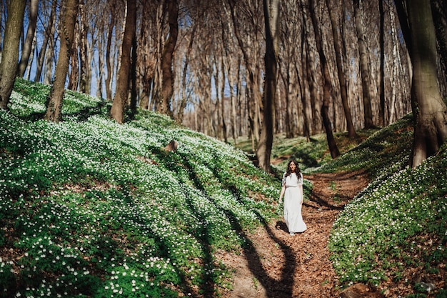 Kijk van veraf naar de vrouw in het wit wandelen in het groene bos