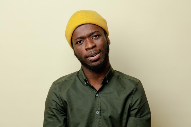 Kijkend naar camera jonge Afro-Amerikaanse man in hoed met groen shirt geïsoleerd op een witte achtergrond