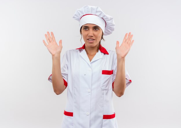 Kijkend naar kant jonge vrouwelijke kok die eenvormige chef-kok draagt die grootte op geïsoleerde witte muur met exemplaarruimte toont
