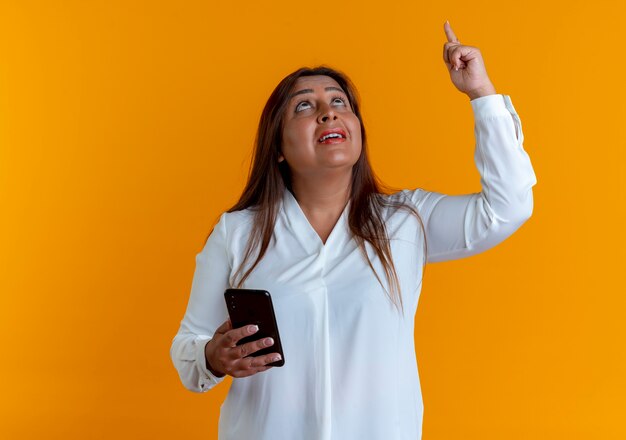 Kijkend naar onder de indruk casual blanke vrouw van middelbare leeftijd met telefoon en wijst naar boven