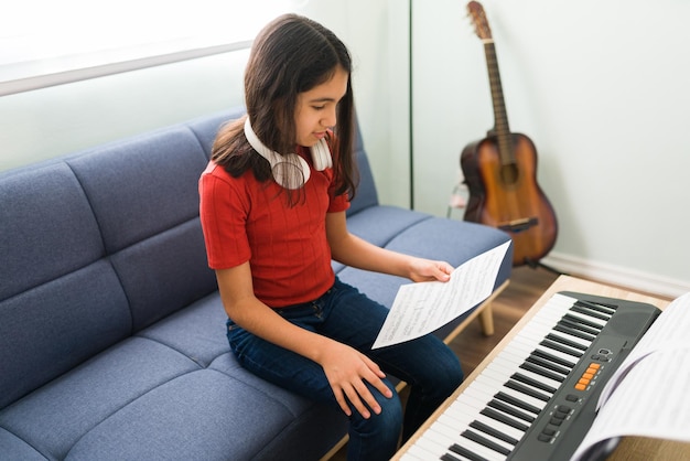 Kind dat het toetsenbord bespeelt. Mooi meisje dat een stuk bladmuziek leest en piano leert spelen terwijl ze haar muzieklessen oefent in de woonkamer