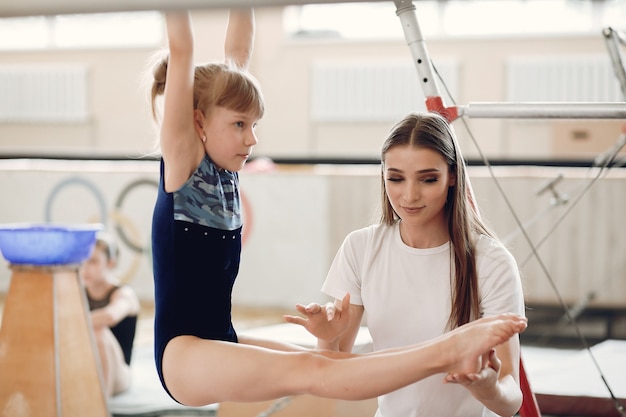 Kind gymnastiek evenwichtsbalk. Meisje gymnast atleet tijdens een oefening horizontale balk in gymnastiek wedstrijden. Coach met kind.