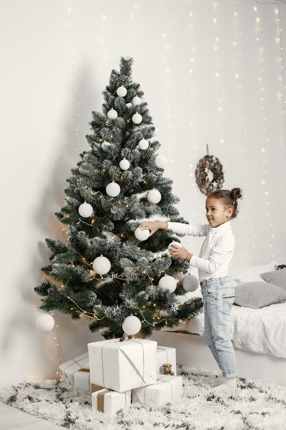 Kind in een witte trui. Dochter die zich dichtbij Kerstboom bevindt.