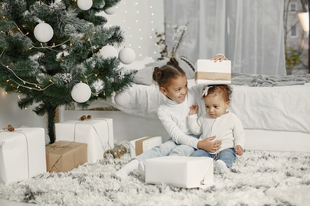 Kind in een witte trui. Dochters stitting in de buurt van de kerstboom. Twee zussen thuis.