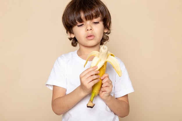 Kind jongen schattig lief in wit t-shirt peeling banaan op roze muur