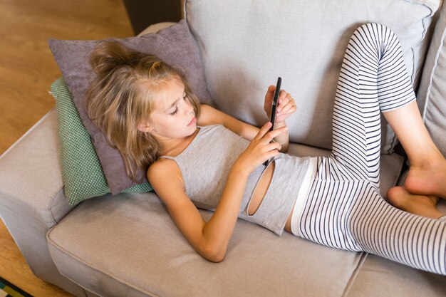 Kind kijkt naar haar telefoon en zit op de bank