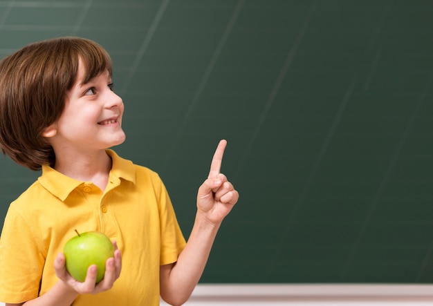 Gratis foto kind met een appel terwijl hij omhoog wijst