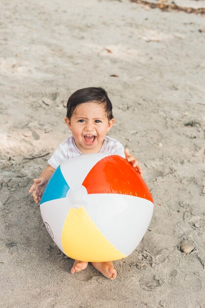 Kind zittend op zand met opblaasbare bal