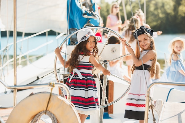 kinderen aan boord van een zeejacht die sinaasappelsap drinken. tiener of kindmeisjes tegen blauwe hemel buiten. Kleurrijke kleding. Concepten voor kindermode, zonnige zomer, rivier en vakantie.