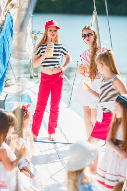kinderen aan boord van een zeejacht die sinaasappelsap drinken. tiener of kindmeisjes tegen blauwe hemel buiten