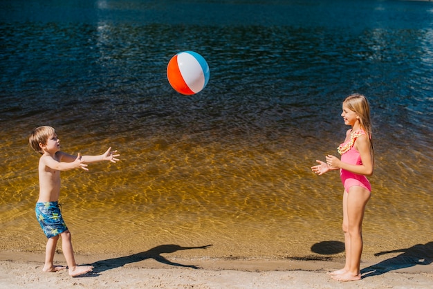 Kinderen die met strandbal spelen die zich dichtbij overzees bevinden
