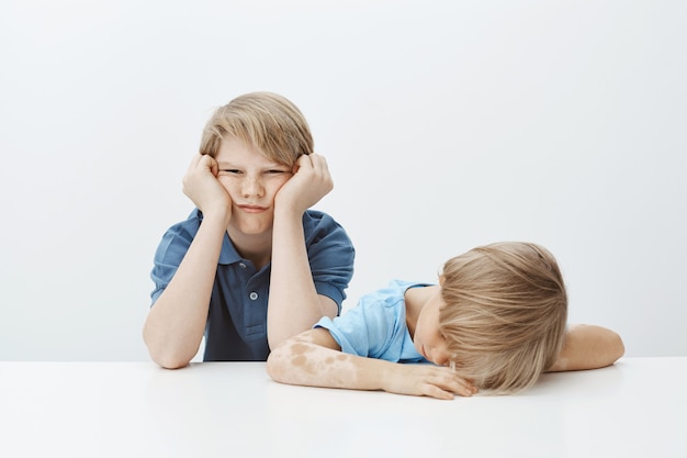 Kinderen die zich vervelen, willen spelen in plaats van huiswerk te maken. portret van onverschillige sombere broerzitting met broer of zus