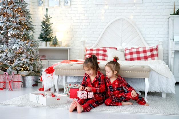 Kinderen in geruite pyjama pakken cadeautjes uit op de vroege kerstochtend op de grond bij het bed