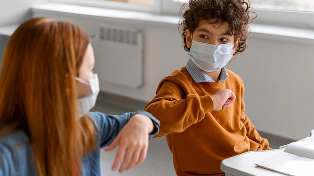 Kinderen met medische maskers doen de ellebooggroet in de klas