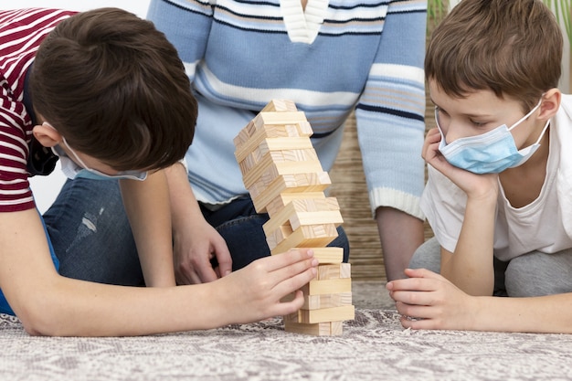 Gratis foto kinderen met medische maskers spelen jenga met moeder