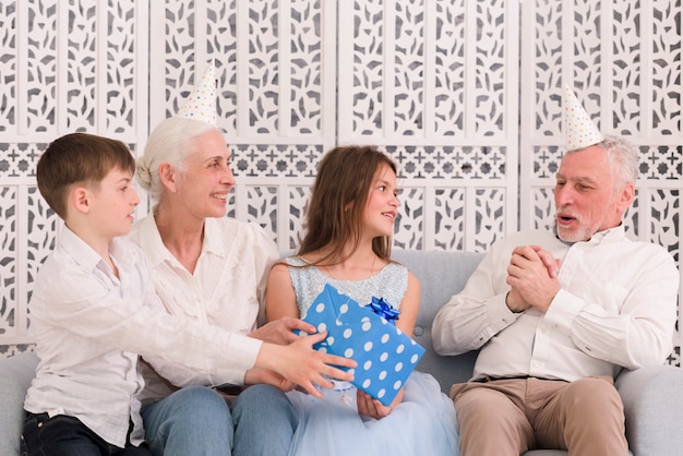 Kinderen met oma geven geschenk aan hun gelukkige grootvader zittend op de Bank