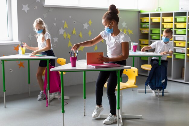 Kinderen staan naast hun bureau terwijl ze medische maskers dragen