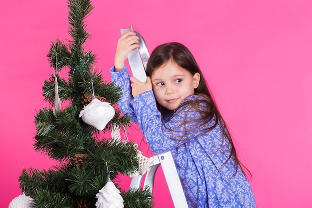 Kinderen vakantie en kerst concept meisje versieren kerstboom op roze achtergrond