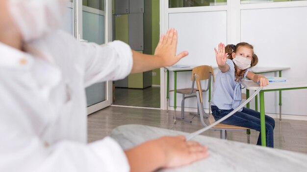 Kinderen zwaaien in de klas terwijl ze afstand houden