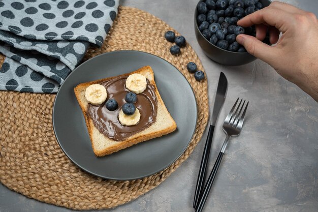 Kinderontbijt of lunch of snacktoast met chocolade-hazelnootpasta, banaan en bosbes in de vorm van een schattig beertje.