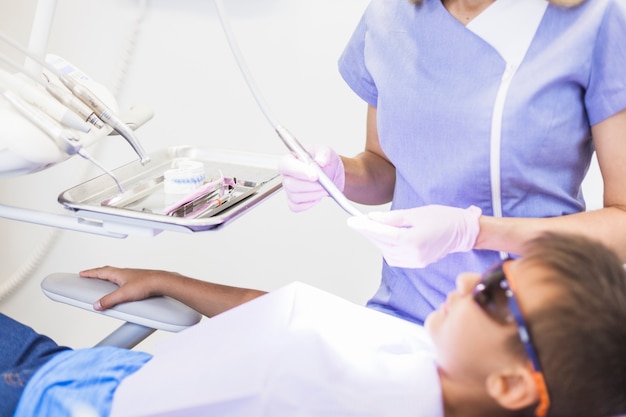 Kindpatiënt die voor tandarts leunen die ultrasone schaler houden