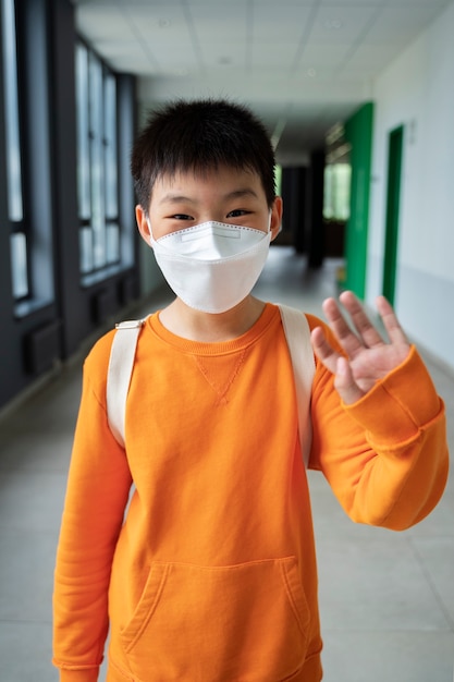 Gratis foto kindstudent met medisch masker dat op school zwaait