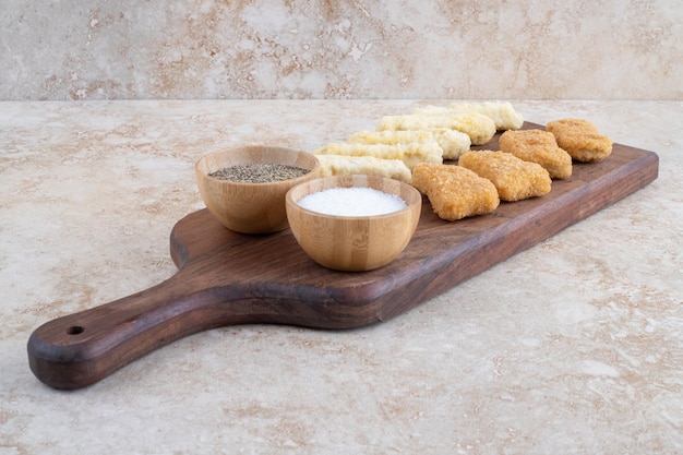 Kipnuggets en kaasstengels op een houten bord met verschillende sauzen eromheen.