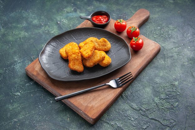 Kipnuggets op een zwarte plaat en vork op houten plank tomatenketchup op donkere ondergrond met vrije ruimte