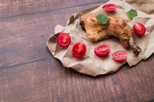 Gratis foto kippenbenen op pakpapier met gehalveerde tomaten op houten lijst