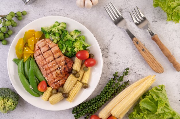 Kippenbiefstuk gegarneerd met witte sesam, erwten, tomaten, broccoli en pompoen in een witte plaat.