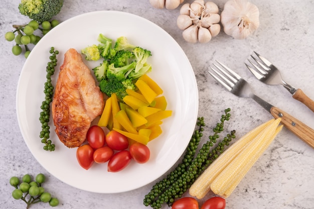 Kippenbiefstuk gegarneerd met witte sesam, erwten, tomaten, broccoli en pompoen in een witte plaat.