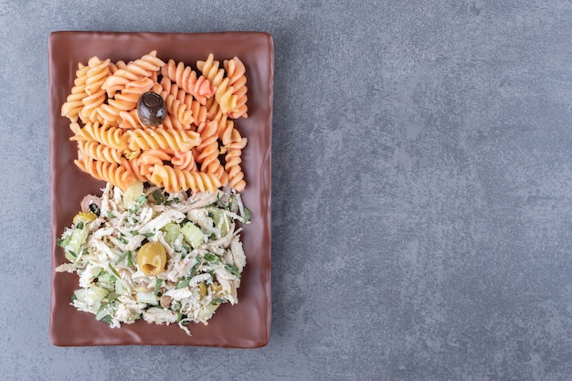 Kippensalade en fusilli pasta op bruine plaat.