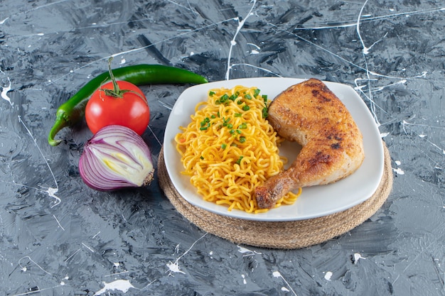 Kippenvlees en noedels op een bord op een onderzetter naast groenten, op de marmeren achtergrond.