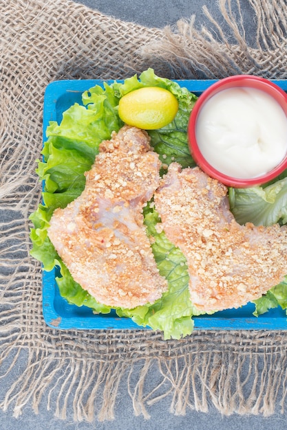 Gratis foto kippenvleugels met broodkruimels en groenten op blauw bord.