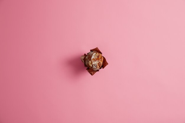 Klaar gebakken muffin gepoederd met suiker in bruin papier geïsoleerd op roze achtergrond. Verse zoetwaren, zoet leven, junkfood-concept. Ontbijt. Dessert voor fijnproevers. Selectieve aandacht.
