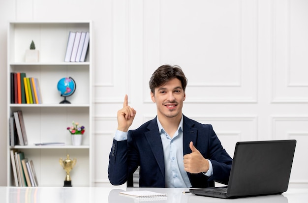 Klantenservice de schattige brunette man in het pak met laptop blij naar boven gericht