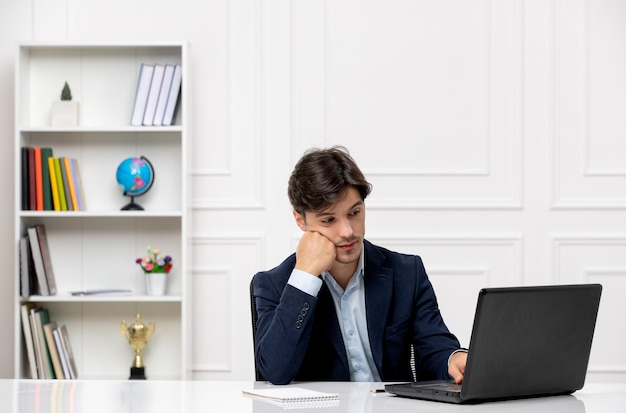 Klantenservice de schattige brunette man in het pak met laptop denkend en kijkend naar display