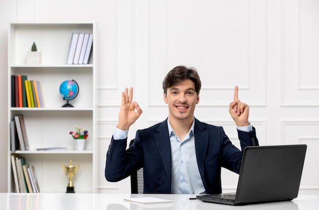 Klantenservice de schattige brunette man in het pak met laptop die een goed gebaar toont