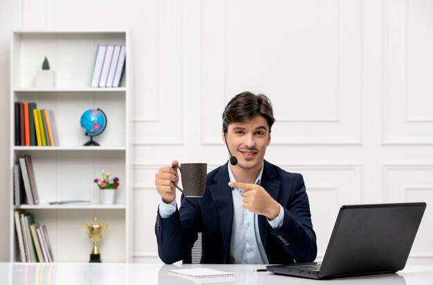 Klantenservice knappe kerel met headset en laptop in pak wijzend op koffiekopje