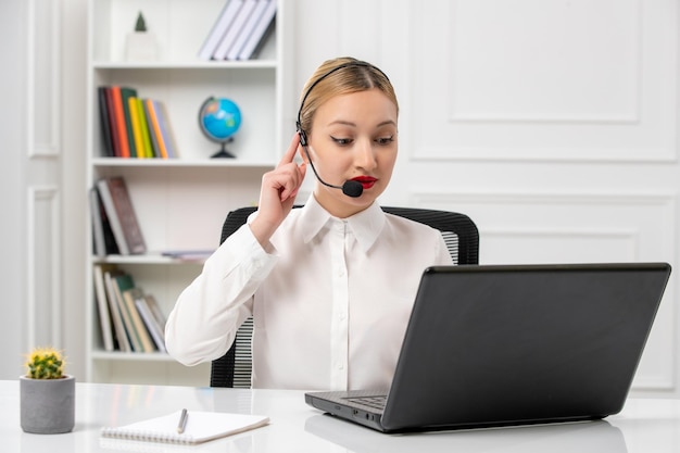 Klantenservice mooi blond meisje in wit overhemd met laptop en headset in gesprek met een klant