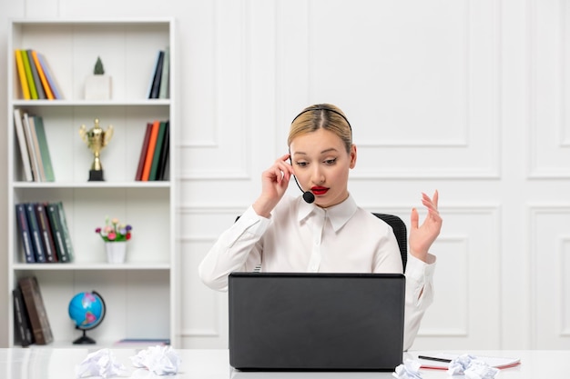 Klantenservice schattig blond meisje office-shirt met headset en computer die zich afvraagt aan de telefoon