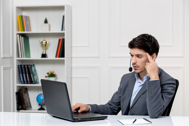 Klantenservice schattige kerel in grijs pak met computer en headset geïrriteerd aanraken van tempels