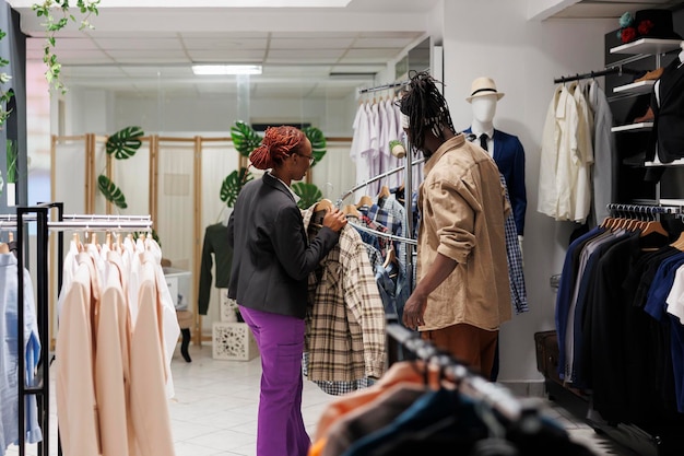 Kledingwinkelassistent helpt klant bij het kiezen van een overhemd op de kledingafdeling van het winkelcentrum. Mode boutique afro-amerikaanse vrouw trendy kledingstuk tonen aan man klant
