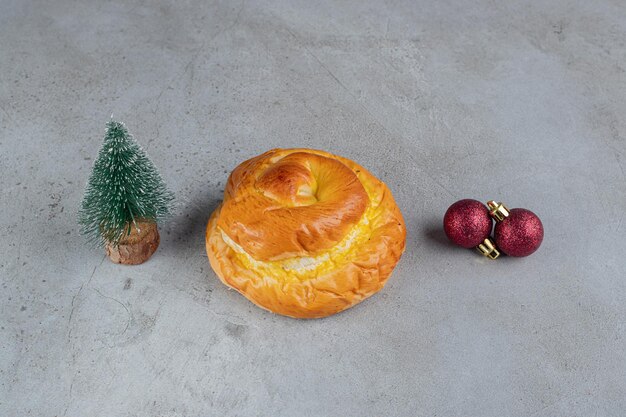 Klein boombeeldje, zoet broodje en decoratieve ballen gerangschikt op marmeren tafel.